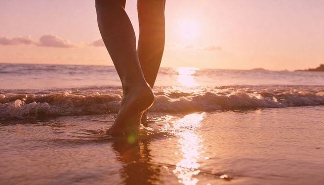 Barefoot woman walking along glowing sunset shoreline with gentle waves and reflections