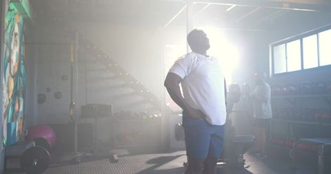 African american man standing hands on hips in backlit industrial gym haze showing power