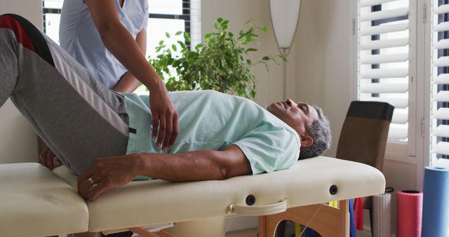 Senior man receiving physical therapy at home from a healthcare professional. This image can be used for illustrating home healthcare services, physical rehabilitation, elderly care programs, wellness practices, advertisements for medical or physiotherapy clinics, and healthcare professional training materials.