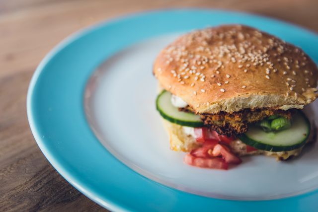 Featuring a well-presented veggie burger with crunchy cucumbers, fresh tomatoes, and a sesame seed bun. Ideal for food blogs, healthy eating promotions, vegetarian lifestyle articles, or recipe websites showcasing homemade meals. Perfect for conveying fresh, healthy, and appetizing food options.
