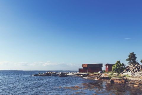 Scandinavian red boathouses standing on rocky shoreline with calm sea and clear blue sky