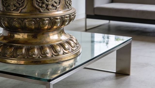 Ornate bronze pedestal with patina on glass coffee table reflecting modern interior