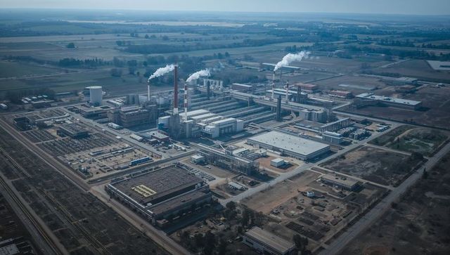 Aerial industrial complex spanning plain with smokestacks emitting steam and pipelines