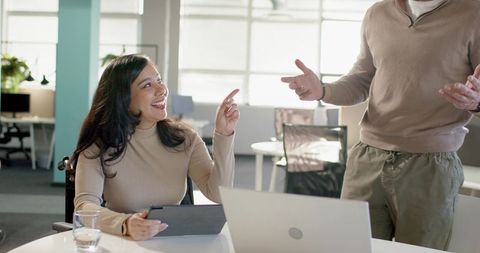 Smiling diverse coworkers collaborating over tablet in bright modern open-plan office daylight
