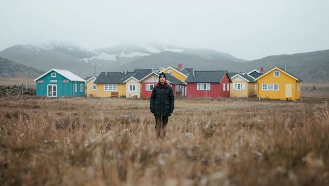 Standing man on windswept plain with colorful cottages and misty mountain backdrop