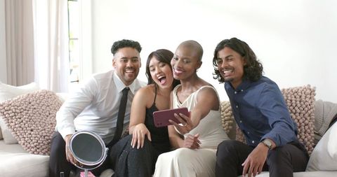 Diverse friends taking selfie on sofa laughing in formal and stylish outfits