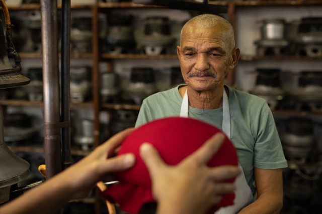 Front view of a senior biracial man looking at making of a new red hat in the workshop at a hat factory