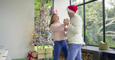 Senior Couple Dancing Joyfully Beside Frosted Christmas Tree and Gifts in cozy Living Room