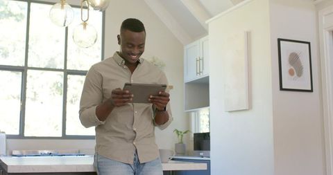Smiling African American man using tablet at bright modern kitchen island home scene