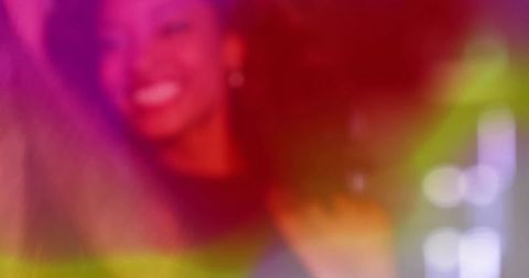 Smiling woman dancing under neon lights with curly hair, colorful bokeh