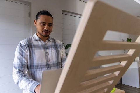 Man working at standing desk with laptop and wooden privacy panel in minimalist home office