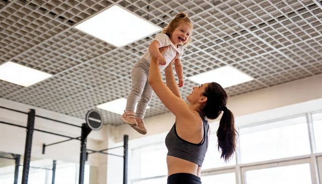 Woman lifting toddler overhead during gym workout showing joyful parent-child bonding