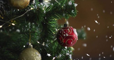 Hanging red christmas bauble with gold swirls on evergreen branch with warm bokeh