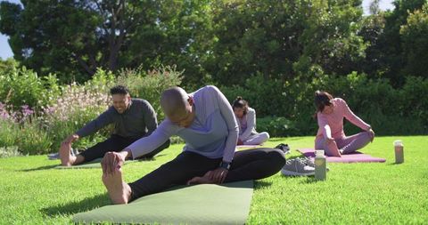 African american friends stretching together on sunny park lawn with yoga mats and water bottles