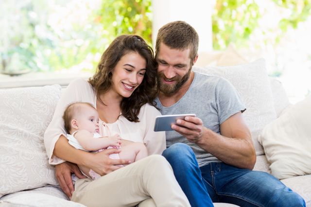 Family sitting on sofa using mobile phone in living room