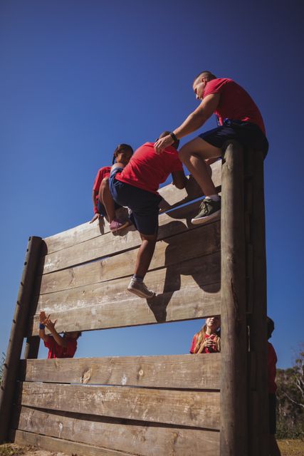 Trainer assisting kids to climb a wooden wall during obstacle course training at boot camp