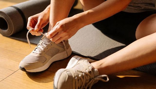 Woman tying beige sneakers on yoga mat preparing for workout