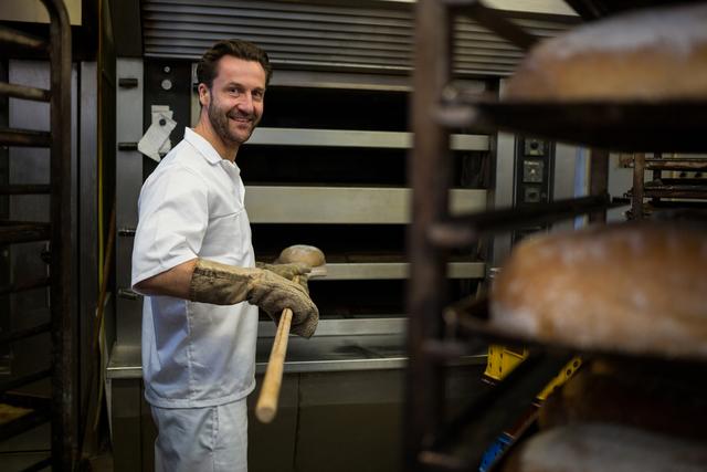 Portrait of smiling baker removing baked bun from oven