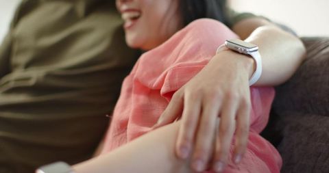 Couple cuddling on sofa laughing woman wearing smartwatch intimate closeup affection