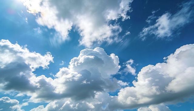 Sunlit cumulus clouds rising and drifting across expansive blue sky with cirrus streaks