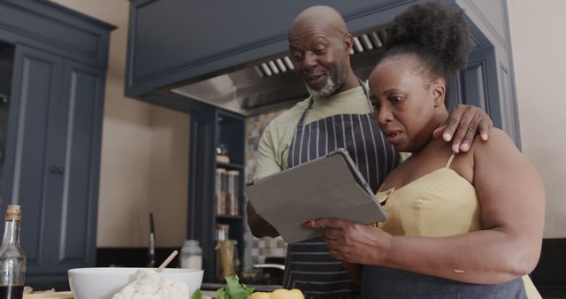 Couple in aprons cooking together and looking at tablet in modern kitchen - Download Free Stock Images Pikwizard.com