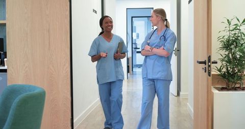 Diverse nurses walking and talking in modern clinic corridor wearing light blue scrubs