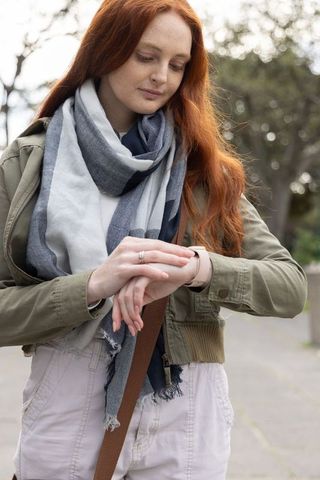 Young woman checking smartwatch and adjusting strap while walking tree-lined path