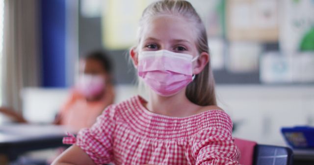 Portrait of caucasian schoolgirl wearing face mask, sitting in classroom looking at camera. children in primary school during coronavirus covid 19 pandemic.