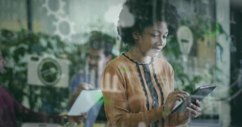 Young black woman tapping tablet in modern open-plan office with frosted glass partition