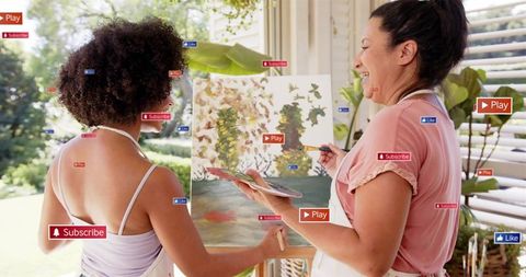 Women painting together on large canvas in sunlit studio with social media overlays