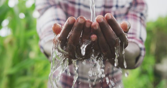 Man collecting fresh water with his cupped hands in outdoor setting. Water flowing steadily with greenery visible in background. Perfect for topics on sustainability, environmental conservation, clean water access, health and lifestyle, and eco-friendly practices.