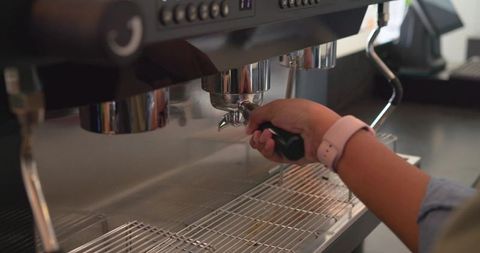 Barista locking portafilter into commercial espresso machine wearing pink wristband