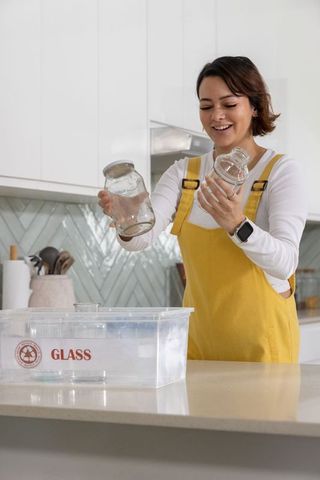 African american woman smiling recycling glass jars in modern kitchen wearing yellow apron