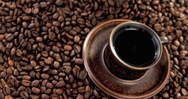 This image shows a rustic coffee cup filled with black coffee, placed among a bed of coffee beans. Ideal for use in cafes, coffee shops, advertisements, marketing materials for coffee brands, or illustrating articles related to coffee culture and lifestyle.