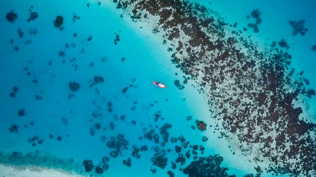 A breathtaking aerial view capturing kayakers navigating through crystal clear blue ocean waters surrounded by reefs. Ideal for travel blogs, tourism promotions, outdoor activity concepts, and ocean preservation campaigns.