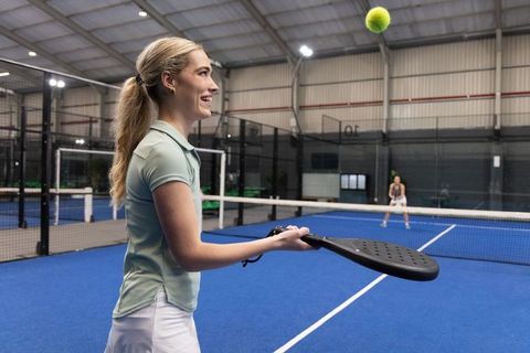 Two women rallying on indoor padel court with perforated paddle watching ball