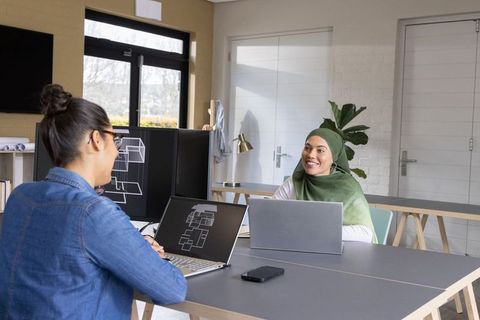 Female architects collaborating over floor plans in bright modern open-plan workspace