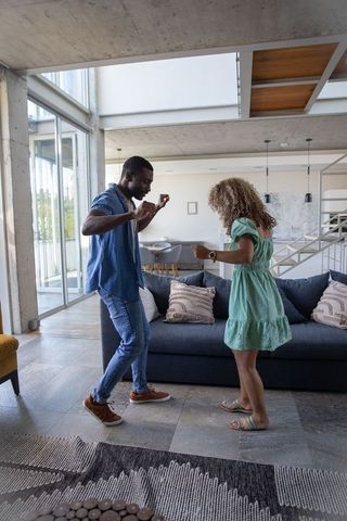 Diverse couple dancing in modern open-plan living room, joyful movement and connection