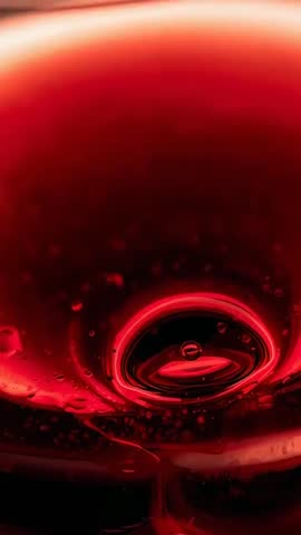Vertical macro video showing red wine rippling and glowing inside glass with central ring