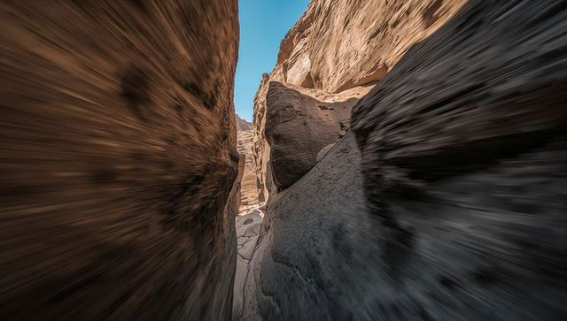 Streaming sun highlighting narrow slot canyon wedged boulder striated sandstone walls