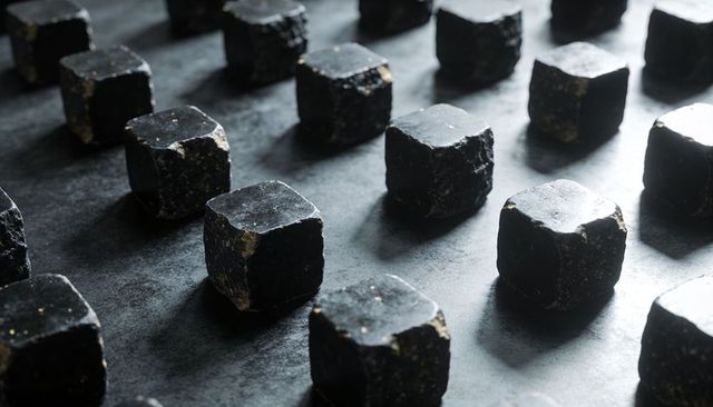 Matte black cubes glinting with gold flecks in geometric grid on dark textured tray