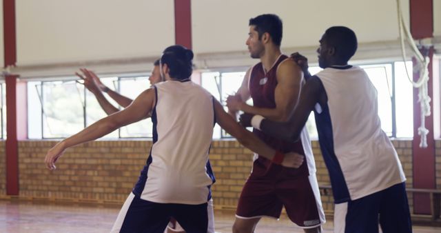 Diverse young men are playing basketball indoors, engaged in a competitive game. Their focus and teamwork highlight the intensity and camaraderie of sports.