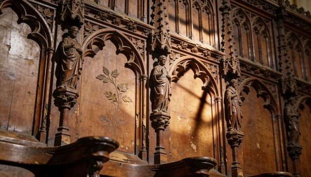 Ornate gothic wooden choir stalls featuring carved saints, tracery and warm sunlight