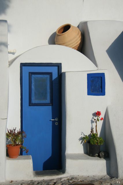 Traditional blue door in whitewashed building captures essence of Greece's Cycladic architecture. Vibrant entrance adorned with potted plants and clay pot. Perfect for promoting Mediterranean destinations, travel blogs, architectural designs, cultural heritage, and lifestyle articles.