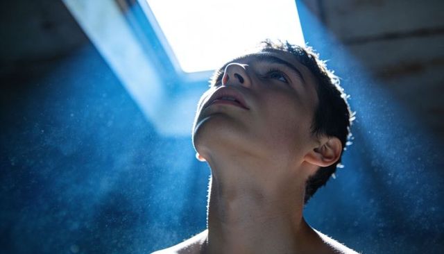 Gazing teen male tilting head toward skylight with sunbeams and dust particles