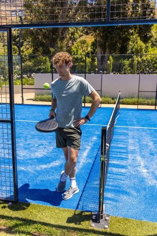 Young man tossing tennis ball while holding padel racket on vibrant blue outdoor court