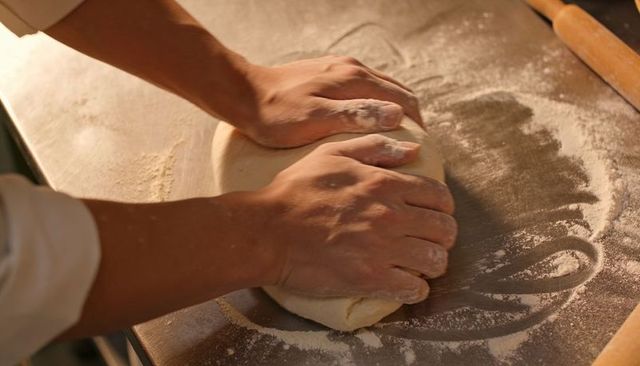 Baker Kneading Dough on Floured Stainless Steel Countertop with Rolling Pin Close-Up