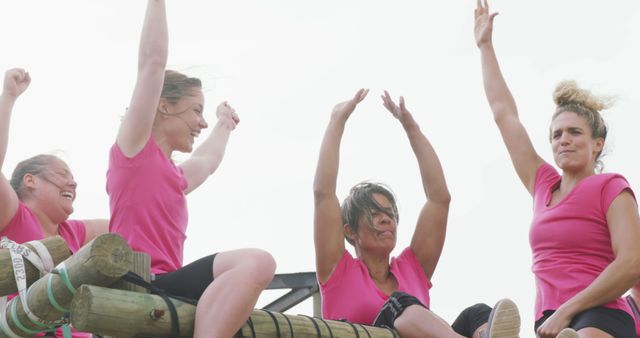 Happy caucasian female friends in pink t shirts celebrating on climbing frame at bootcamp. Female fitness, challenge, friendship and healthy lifestyle.