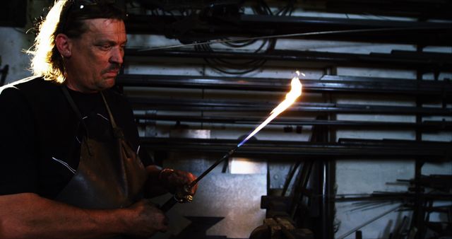 In this workshop, a blacksmith is heating a metal rod with a flame torch. Ideal for illustrating traditional craftsmanship, manual labor, and skilled trades. Useful for websites, articles, and promotional materials related to blacksmithing, traditional crafts, metalworking, and education in trades.