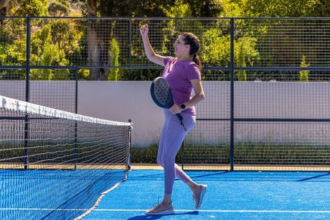 Mature woman celebrating victory on blue padel court holding racket and raising fist
